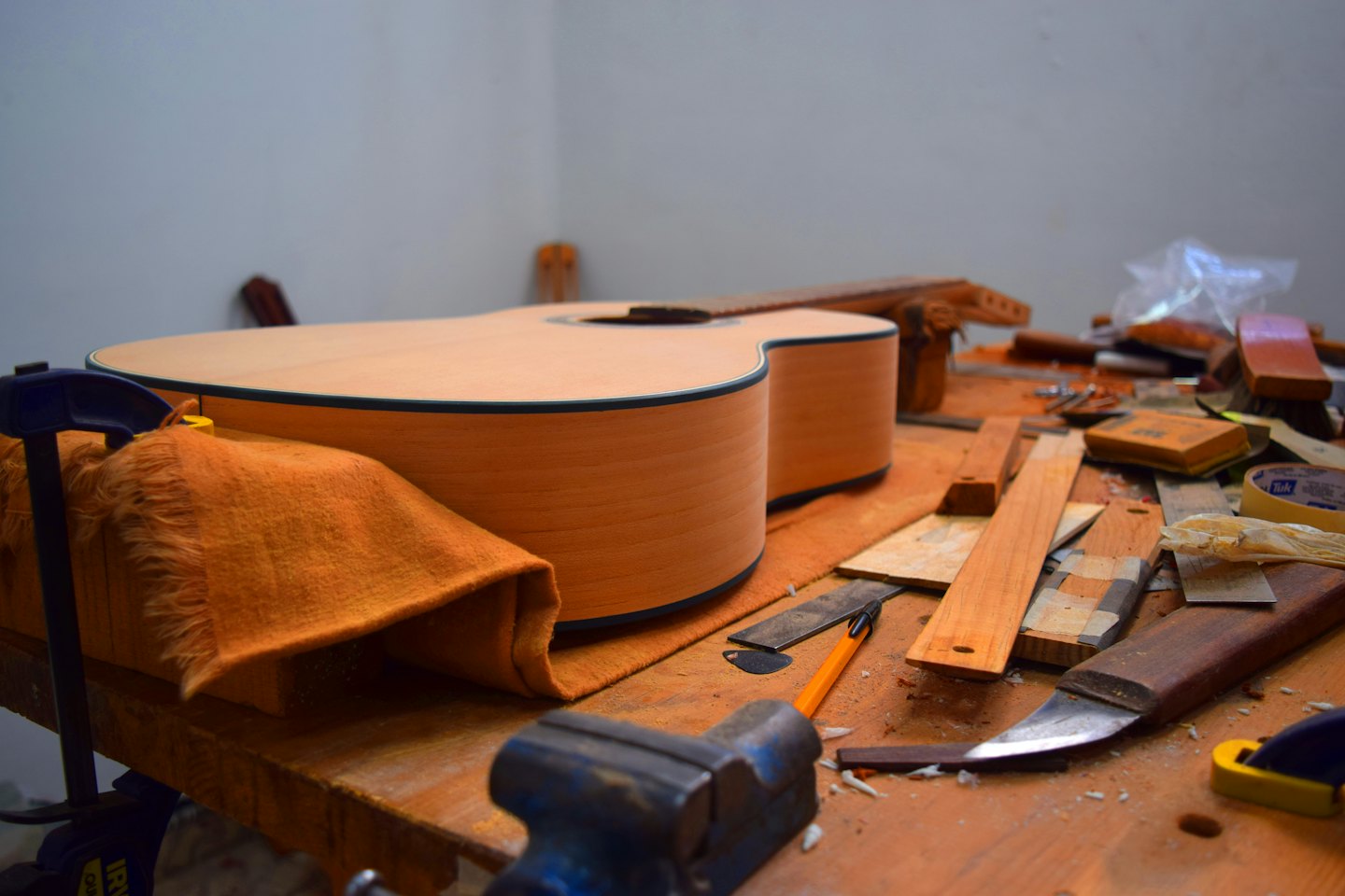 Unfinished acoustic guitar body on a workbench with tools.