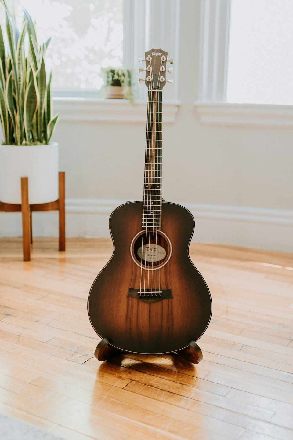 Acoustic guitar standing on a wooden floor in a sunlit room.