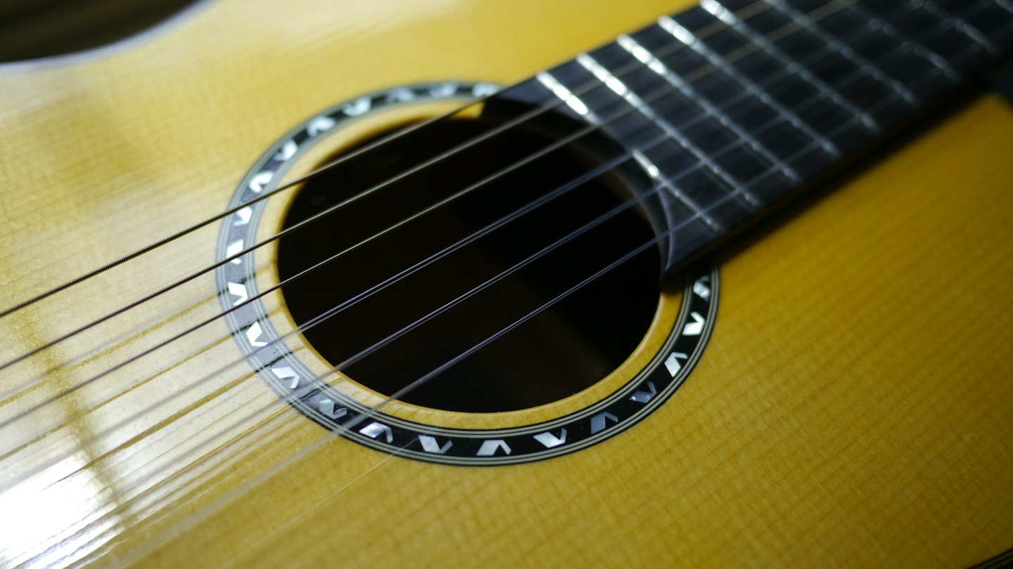Acoustic guitar strings stretch across the decorative wooden soundhole.